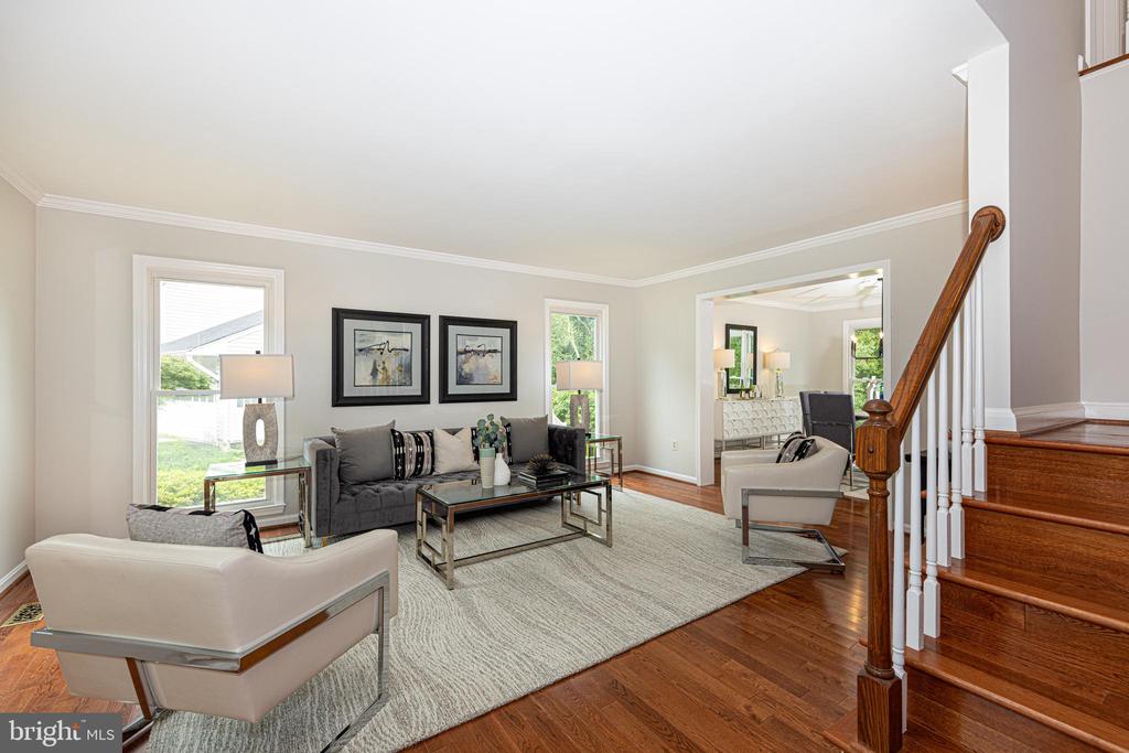 Staged living room with gray sofa, white armchairs, hardwood floors, and a staircase.