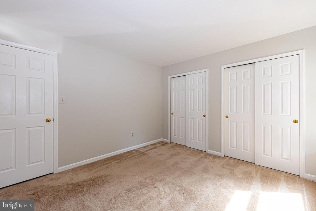 Unfurnished bedroom with beige carpet and several white closet doors.
