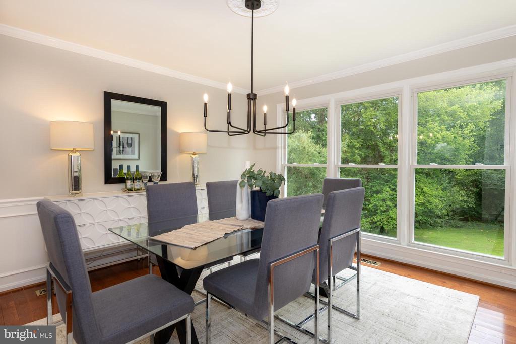 Dining room with a glass-top table, gray chairs, and large windows overlooking trees.