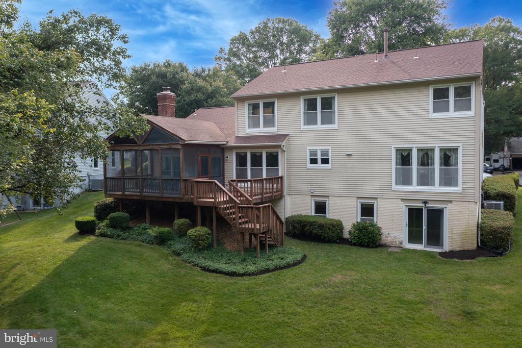Rear of a beige two-story house with a screened porch, raised deck, and landscaped lawn.