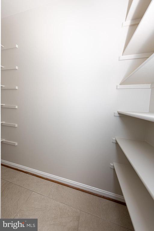 Empty walk-in closet with built-in shelves on both sides and a tiled floor.