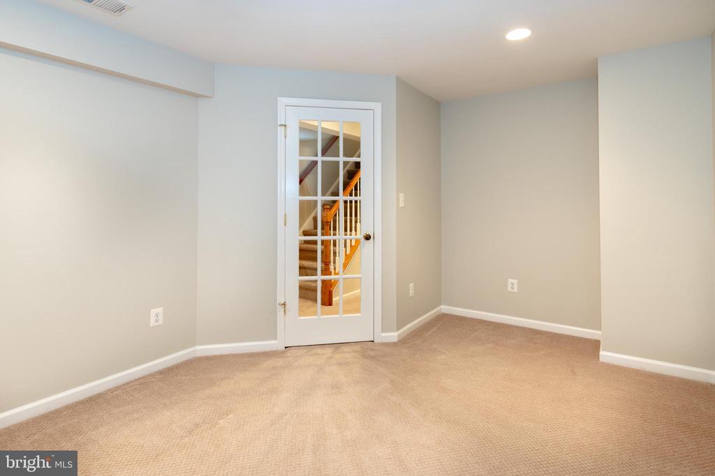 Empty carpeted room with a glass-paneled door opening to a staircase.