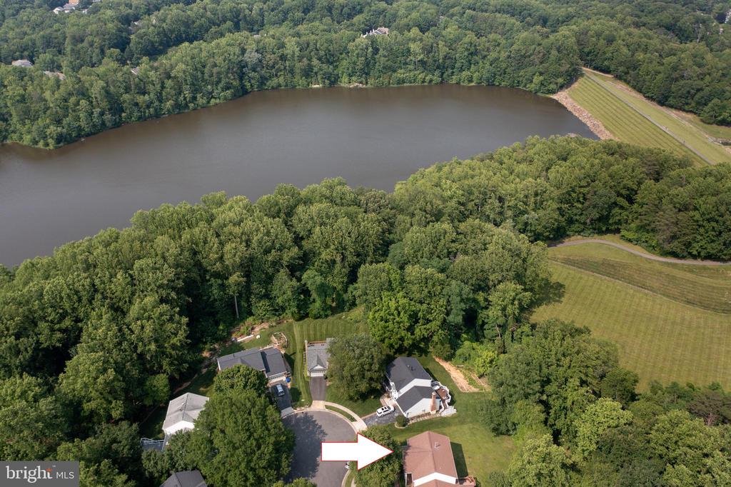 Aerial view of an arrow-marked home beside wooded grounds and a lake.