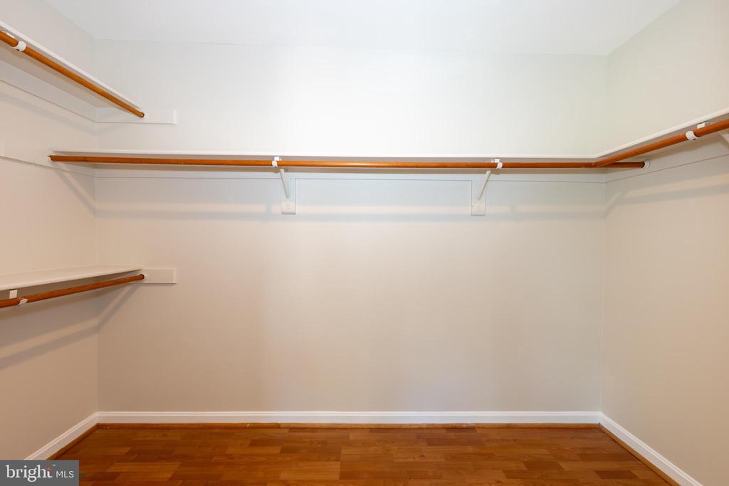 Walk-in closet with wooden hanging rods along three walls and hardwood flooring.