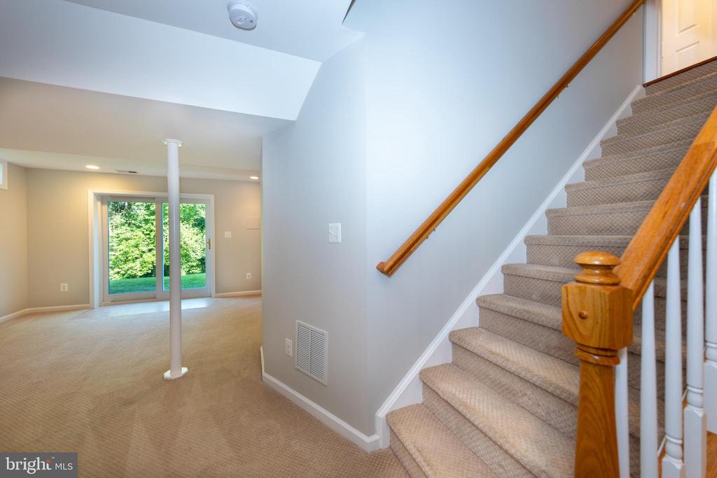 Carpeted lower-level room with a support column, sliding glass doors, and a staircase with wooden handrails.