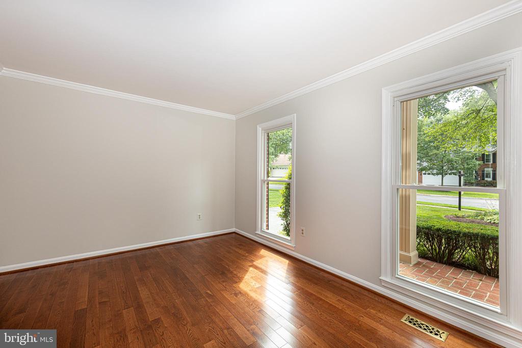 Unfurnished room with polished hardwood floors and two tall windows overlooking greenery.