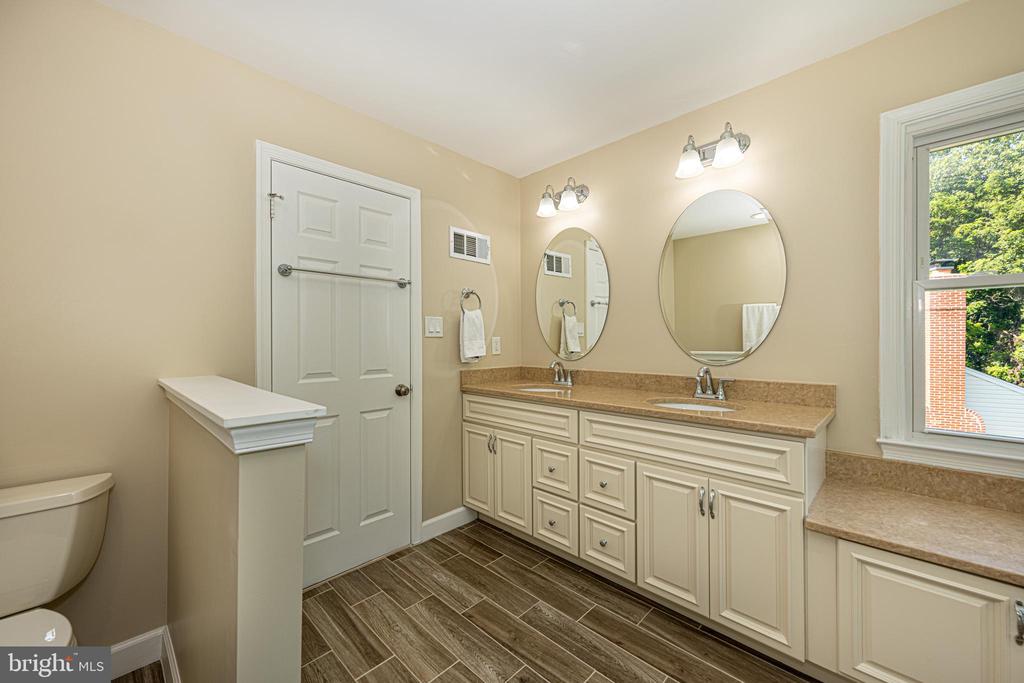 Bathroom with a double-sink vanity, two oval mirrors, and brown tile flooring.