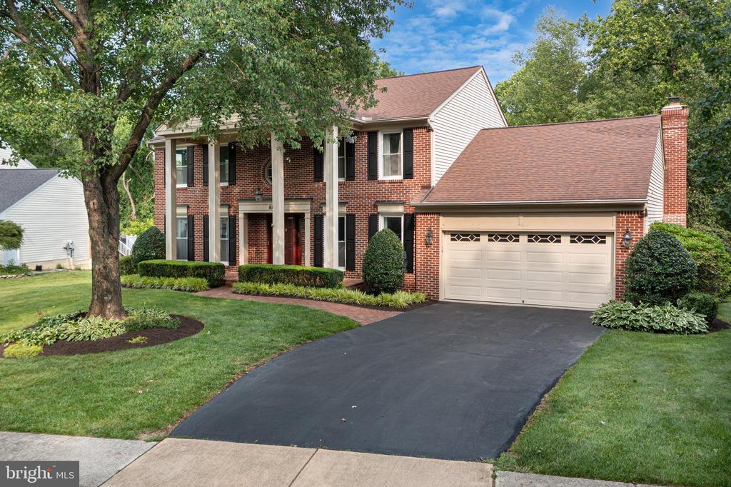 Two-story brick home with a columned entry, attached garage, and landscaped lawn.