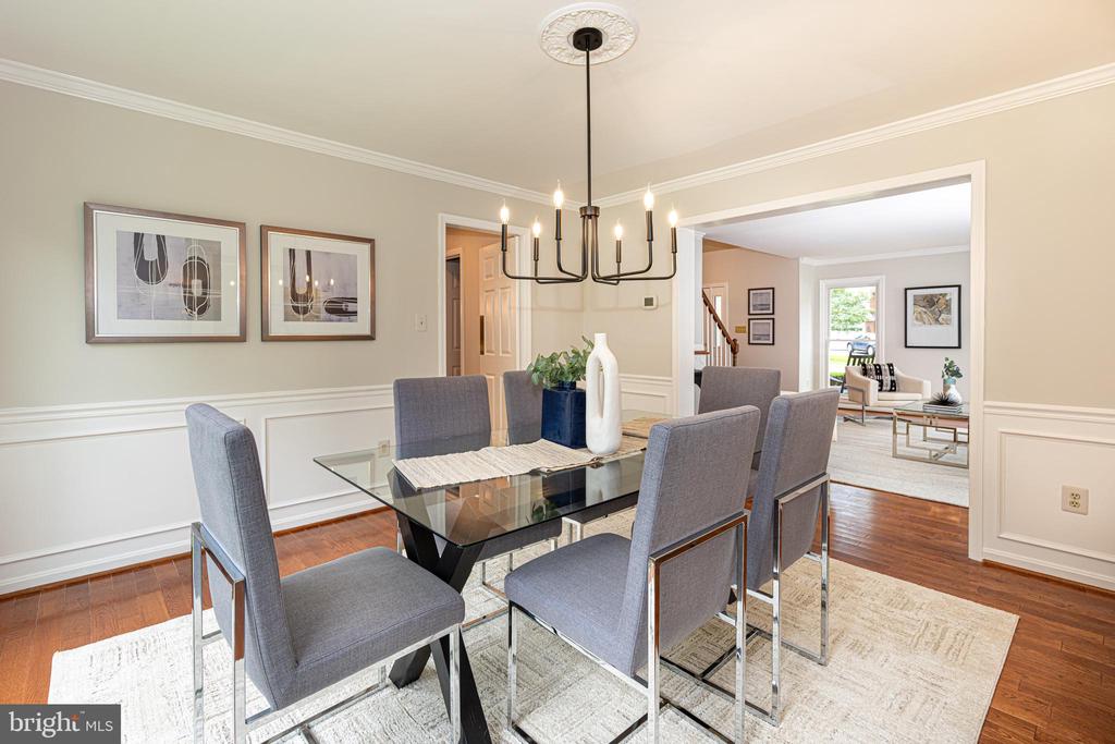 Dining room with a glass-top table, gray chairs, and a chandelier, opening to a bright living room.