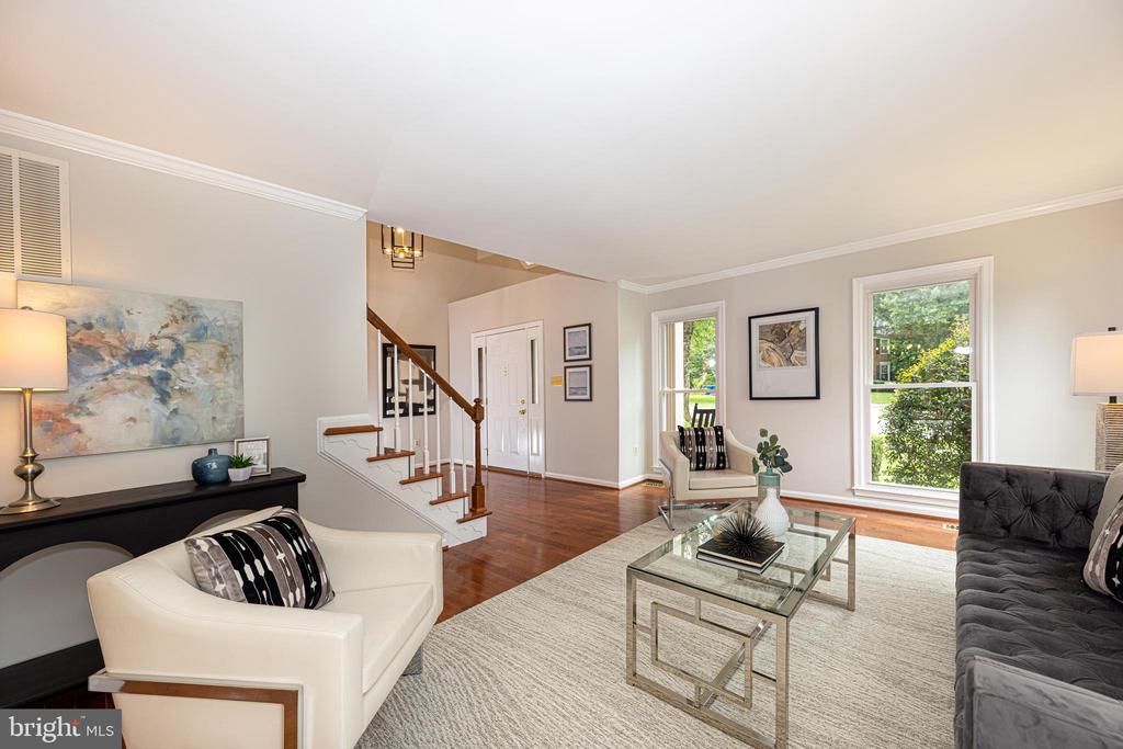 Staged living room with hardwood floors, a staircase, and large windows.
