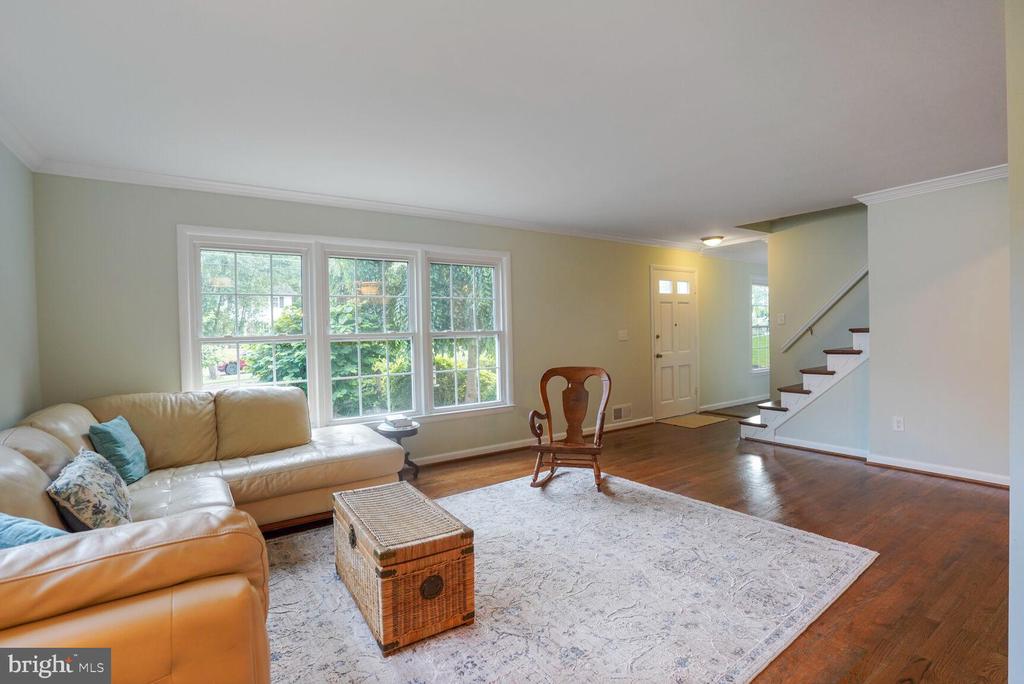 Living room with a cream leather sectional, large windows, hardwood floors, and a staircase.