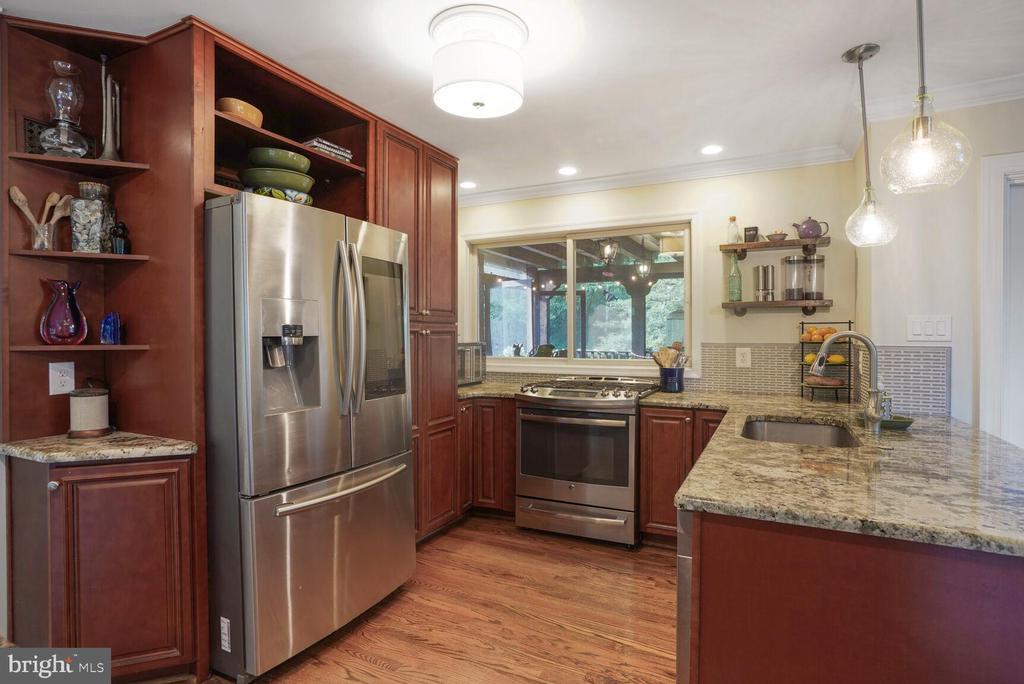 Kitchen with dark wood cabinets, stainless appliances, granite island, and pendant lights.