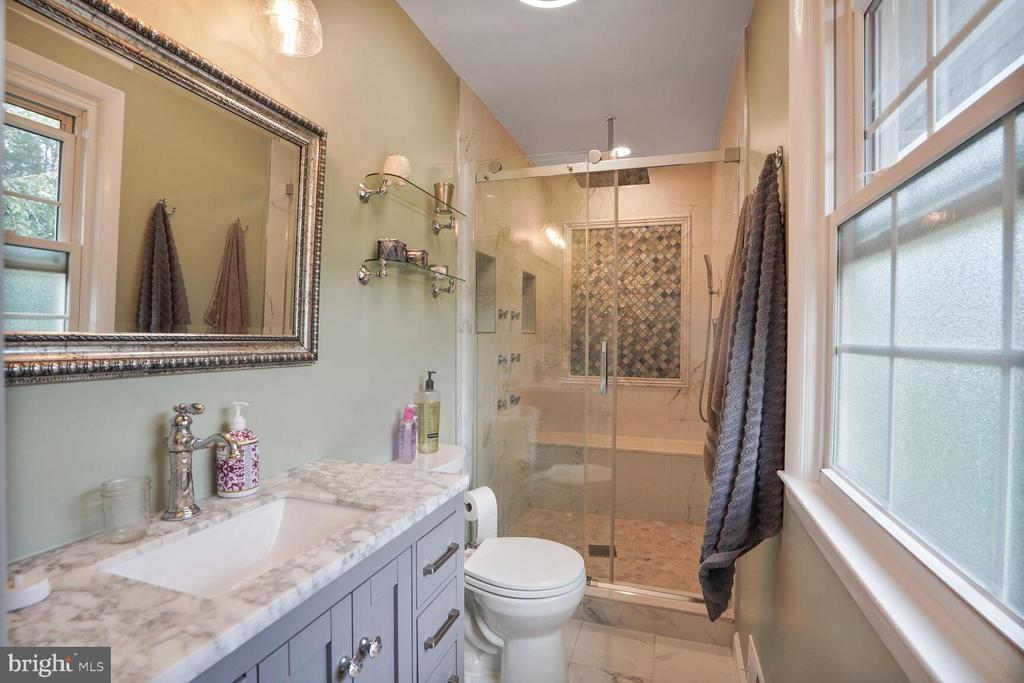 Bathroom with marble vanity, glass shower, patterned tile, and large windows.