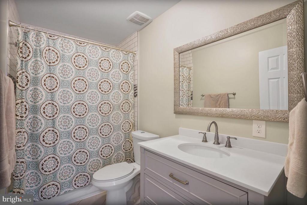 Bathroom with a floral shower curtain, white vanity, and large framed mirror.