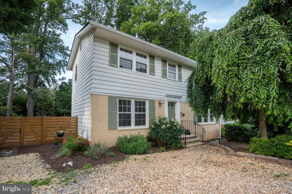 Two-story house with white siding, green shutters, a gravel driveway, and mature trees.