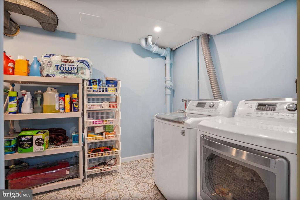 Laundry room with washer, dryer, stocked shelves, and patterned tile flooring.