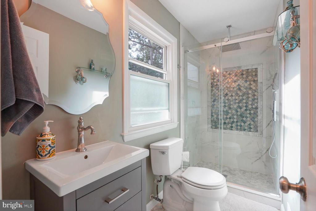 Bathroom with a glass shower featuring a multicolored mosaic tile accent wall and a white vanity.