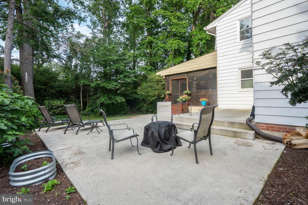 Backyard patio with seating and a covered grill beside a screened porch and mature trees.