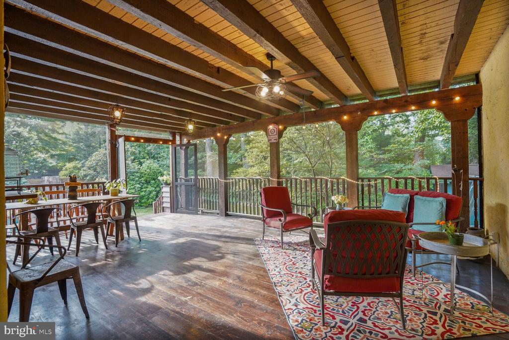 Covered deck with exposed timber beams, dining table, and red lounge chairs overlooking trees.