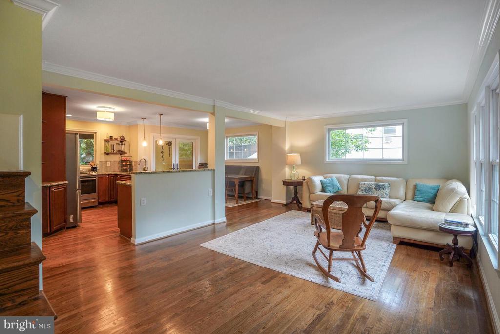Living room with hardwood floors, a white sectional, large windows, and an open kitchen.