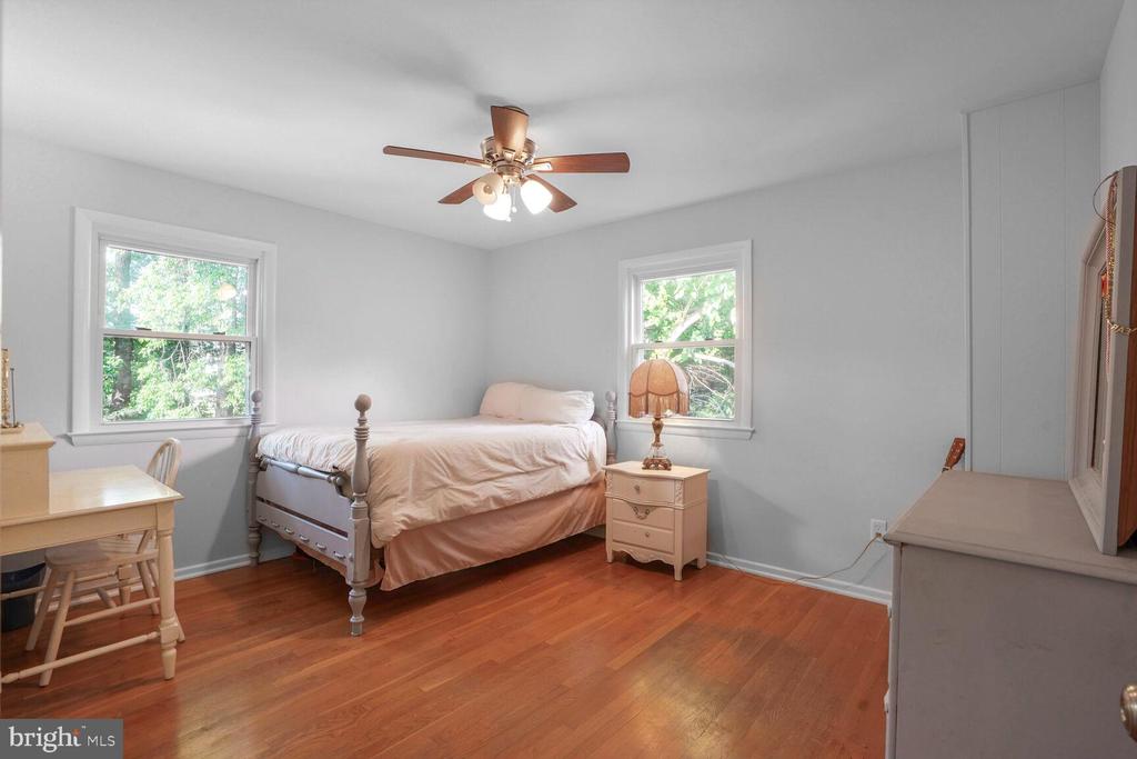 Bedroom with a single bed, hardwood floors, and two windows overlooking leafy trees.