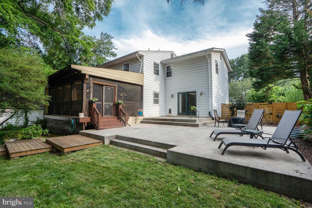 Rear of a two-story home with a screened porch and spacious patio with lounge chairs.