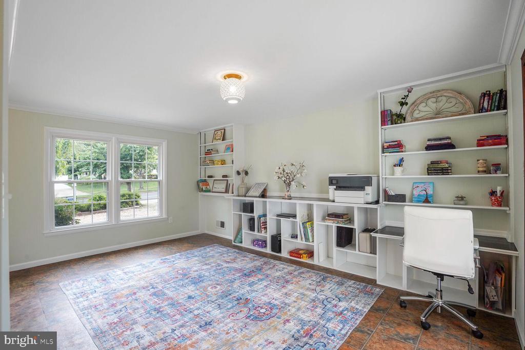 Home office with built-in white bookshelves, large windows, and a colorful patterned rug.