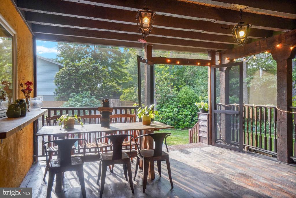 Covered wooden deck with outdoor dining furniture, exposed beams, and views of a leafy garden.