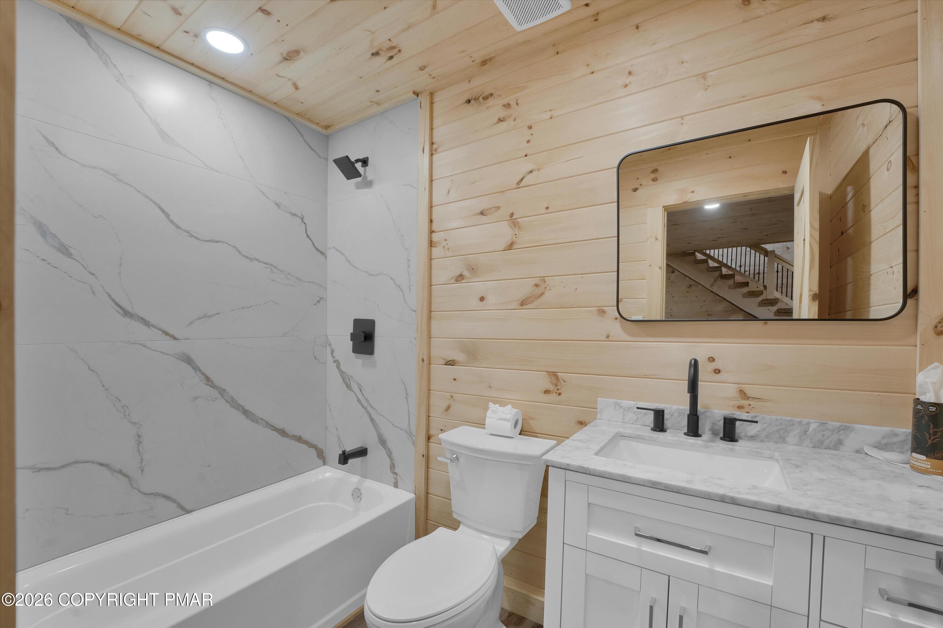 Modern bathroom with marble-look shower walls, a white vanity, and light wood plank walls.