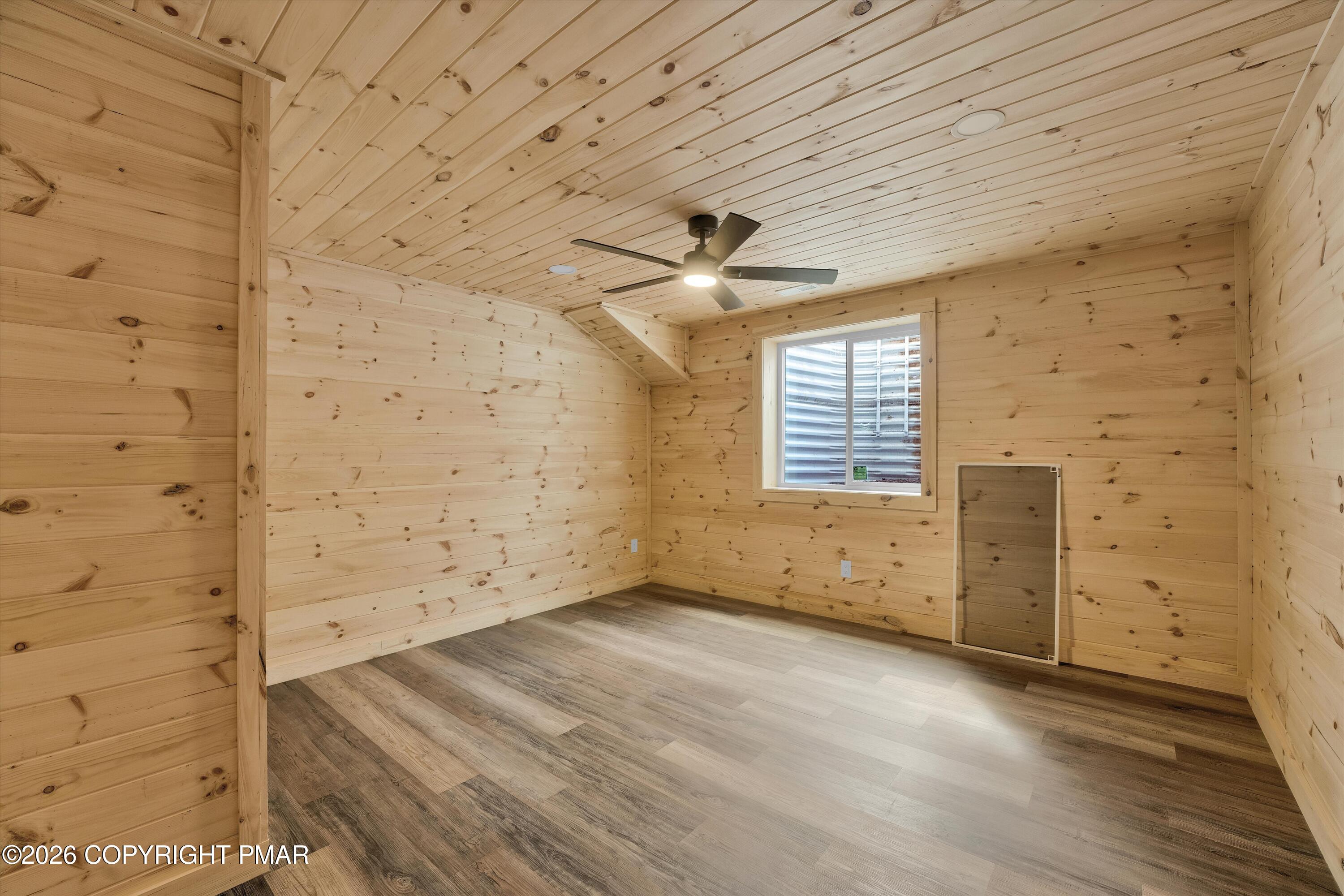 Empty pine-paneled room with a ceiling fan, window, and gray wood-look flooring.