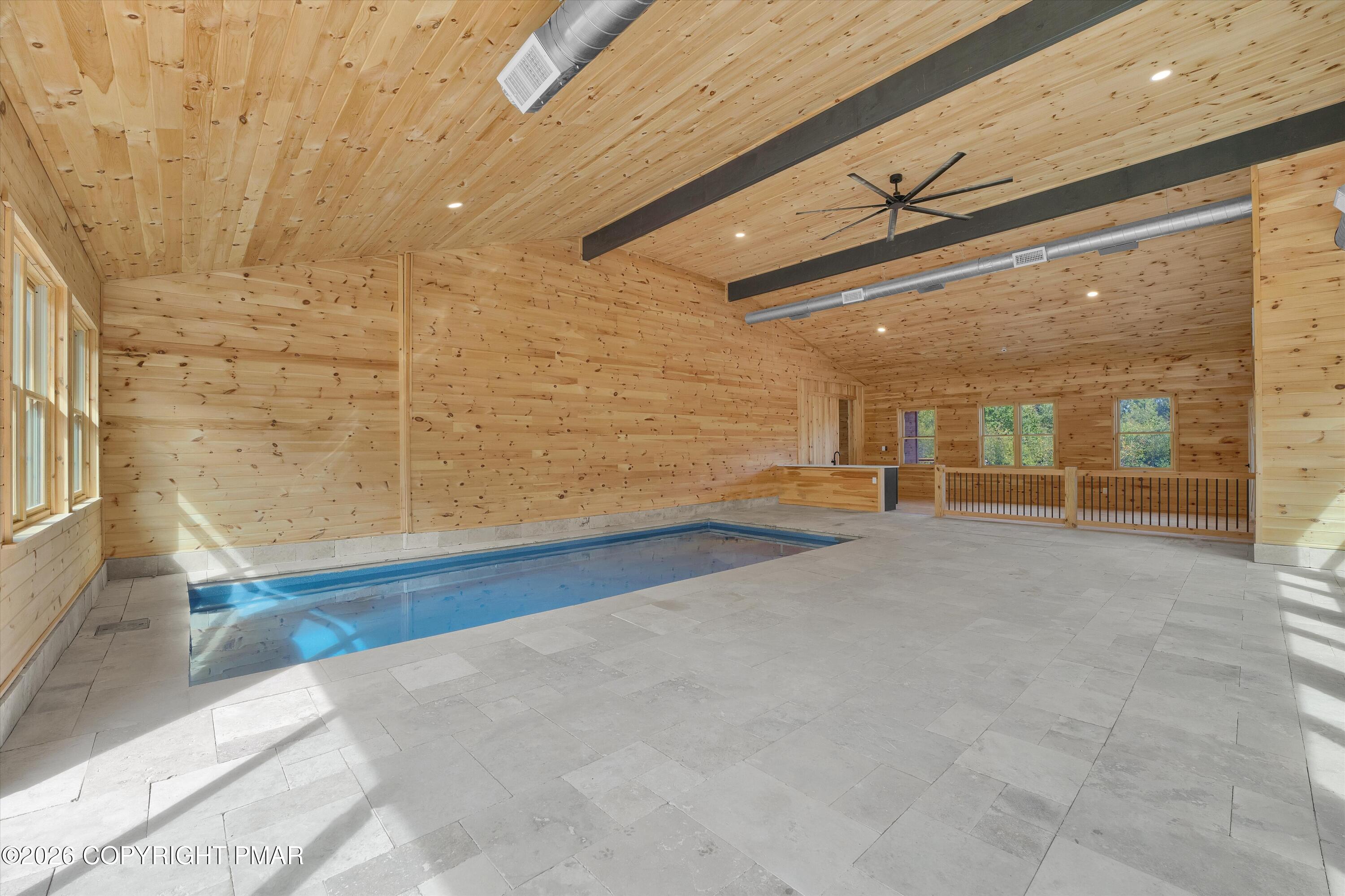 Indoor pool in a spacious wood-paneled room with gray tile flooring and large windows.