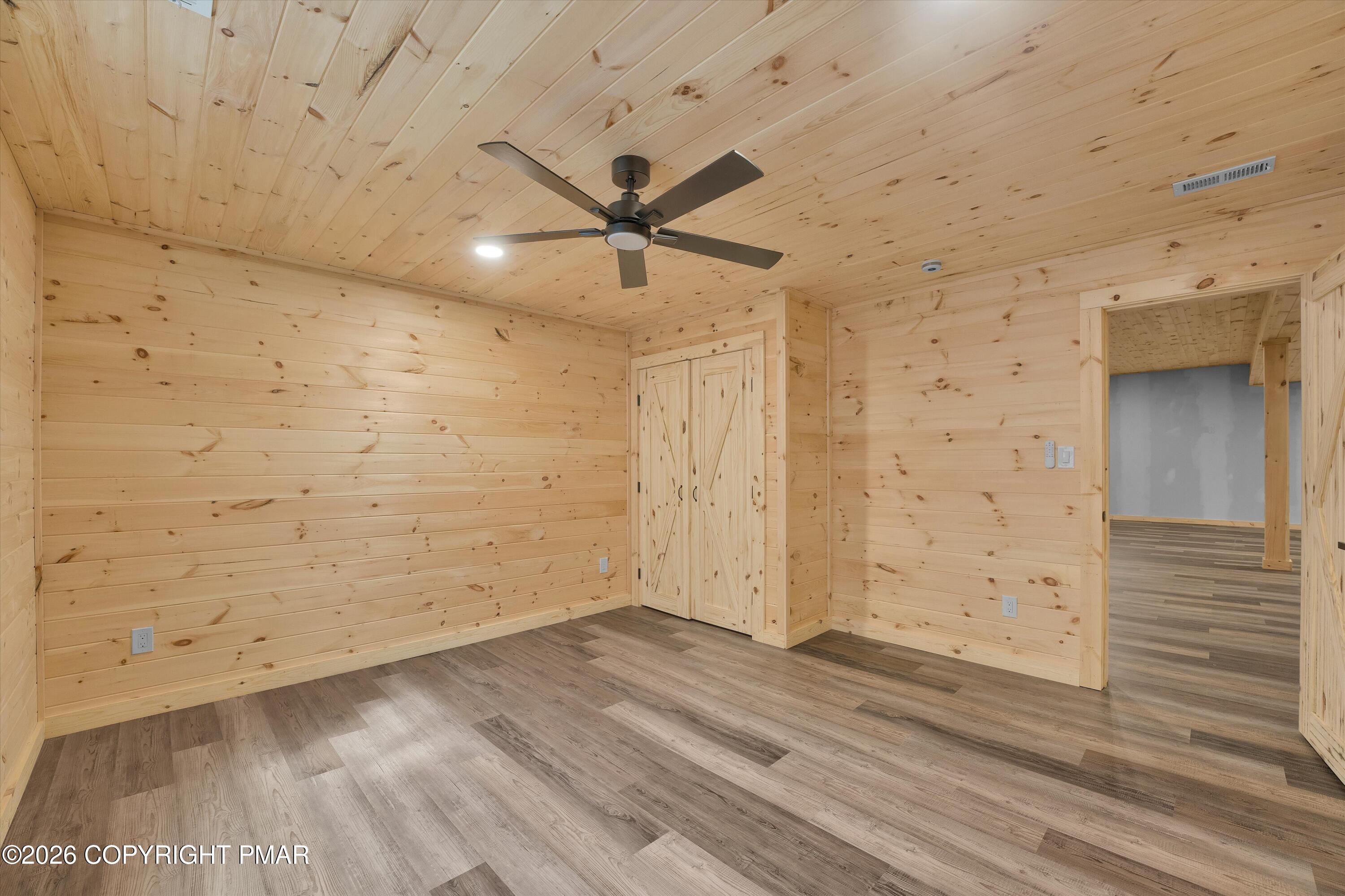 Empty wood-paneled room with a ceiling fan, double closet doors, and plank flooring.