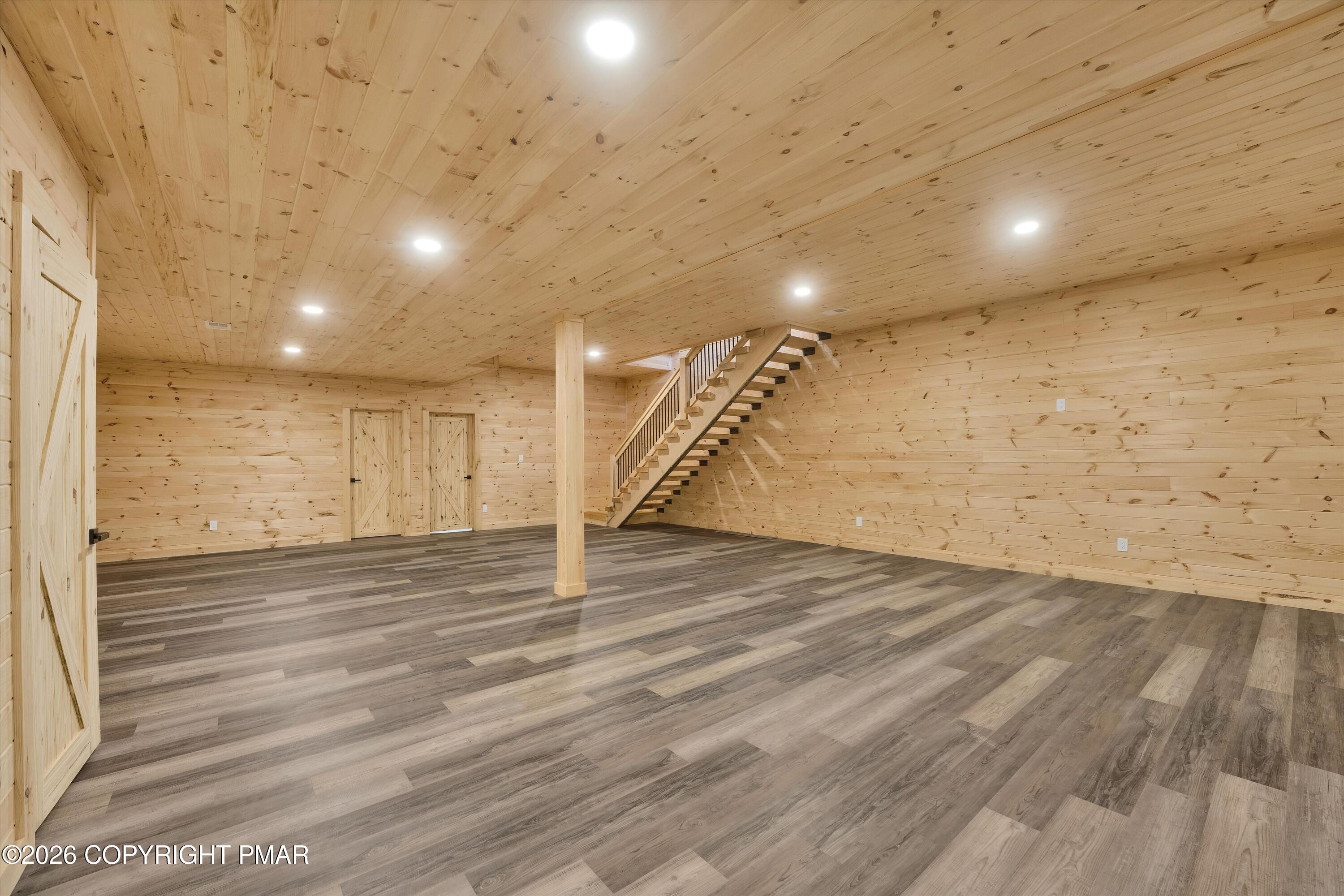 Empty wood-paneled room with gray-brown flooring and an open staircase.