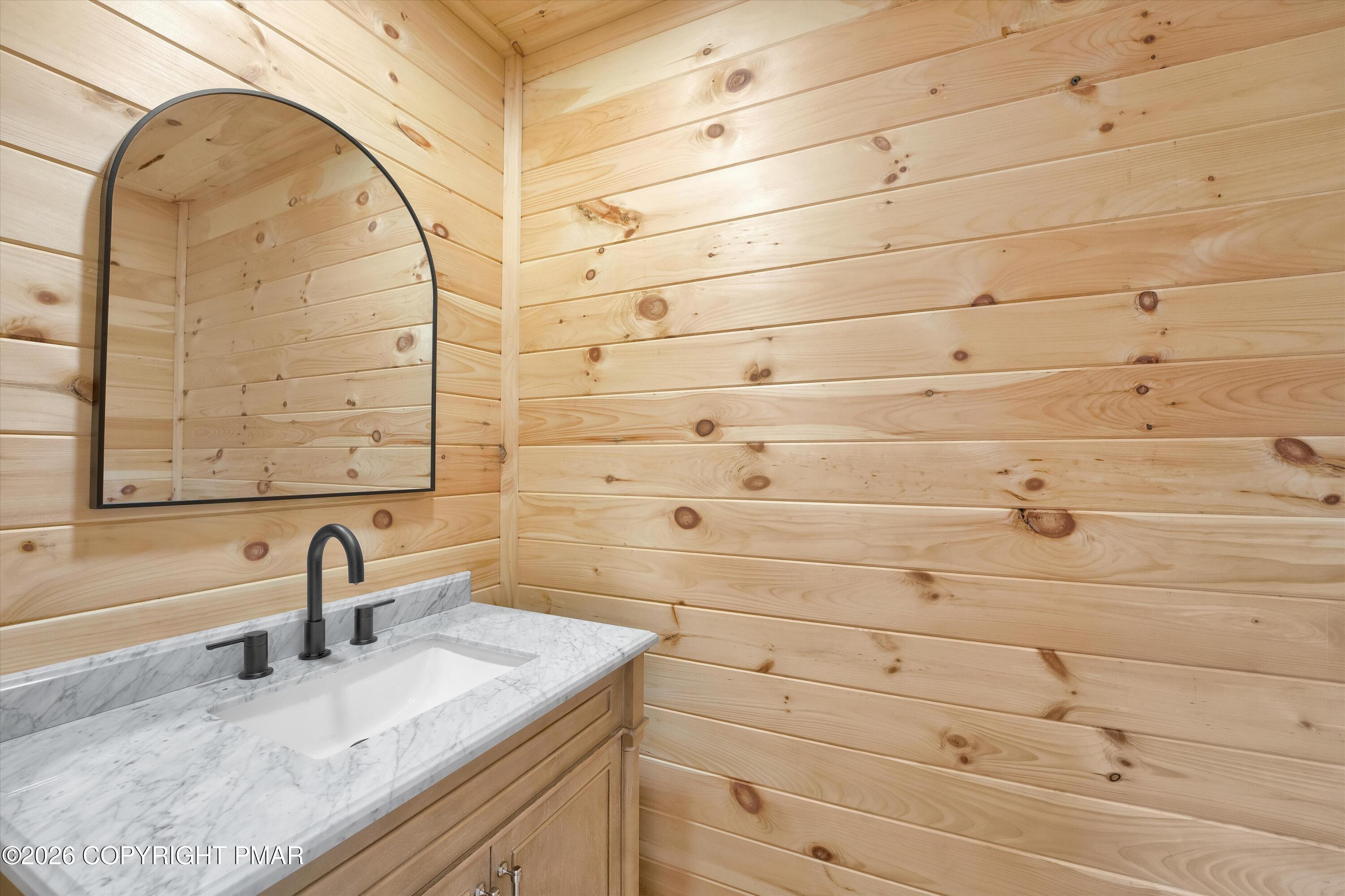 Bathroom vanity with a marble-look counter and arched mirror against knotty pine walls.
