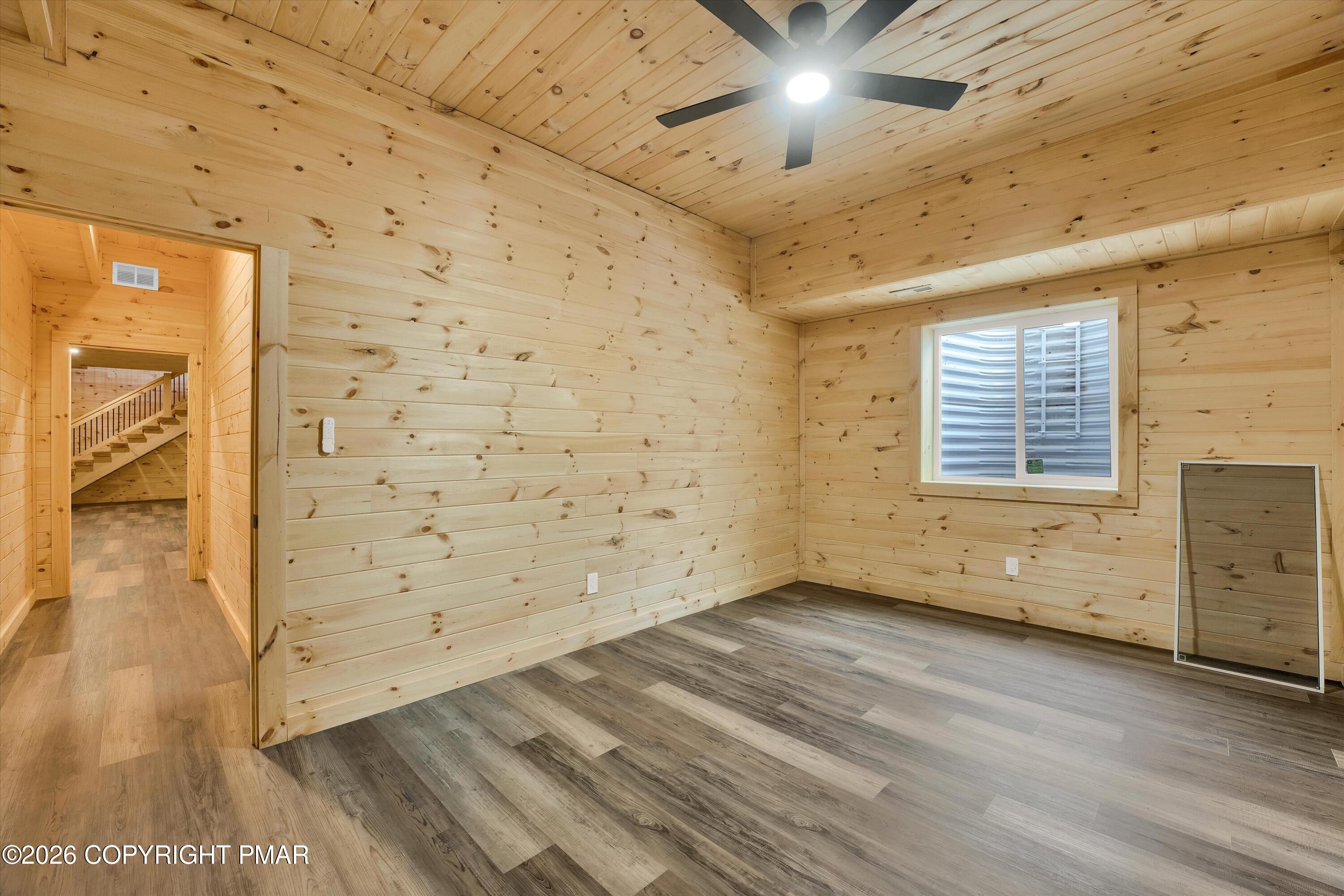 Vacant wood-paneled room with gray plank flooring, a ceiling fan, and a window.