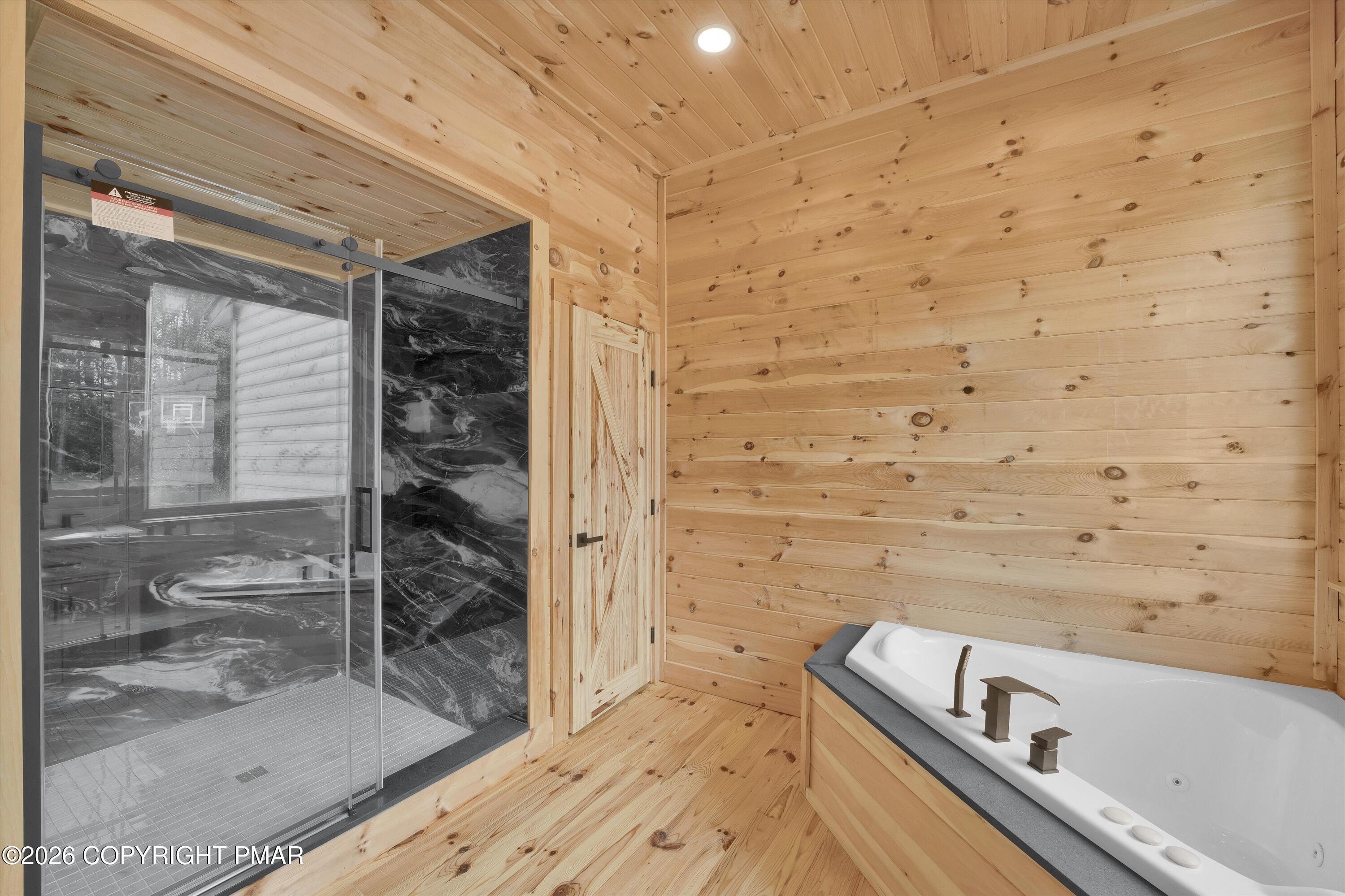 Wood-paneled bathroom with a white jetted tub beside a glass-enclosed, dark-tiled shower.