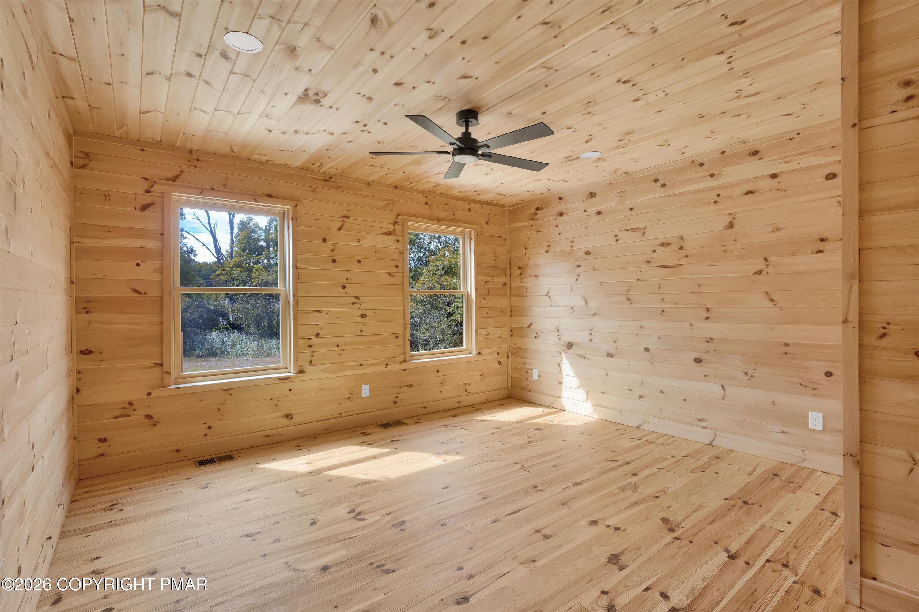 Empty wood-paneled room with plank flooring, two windows, and a ceiling fan.