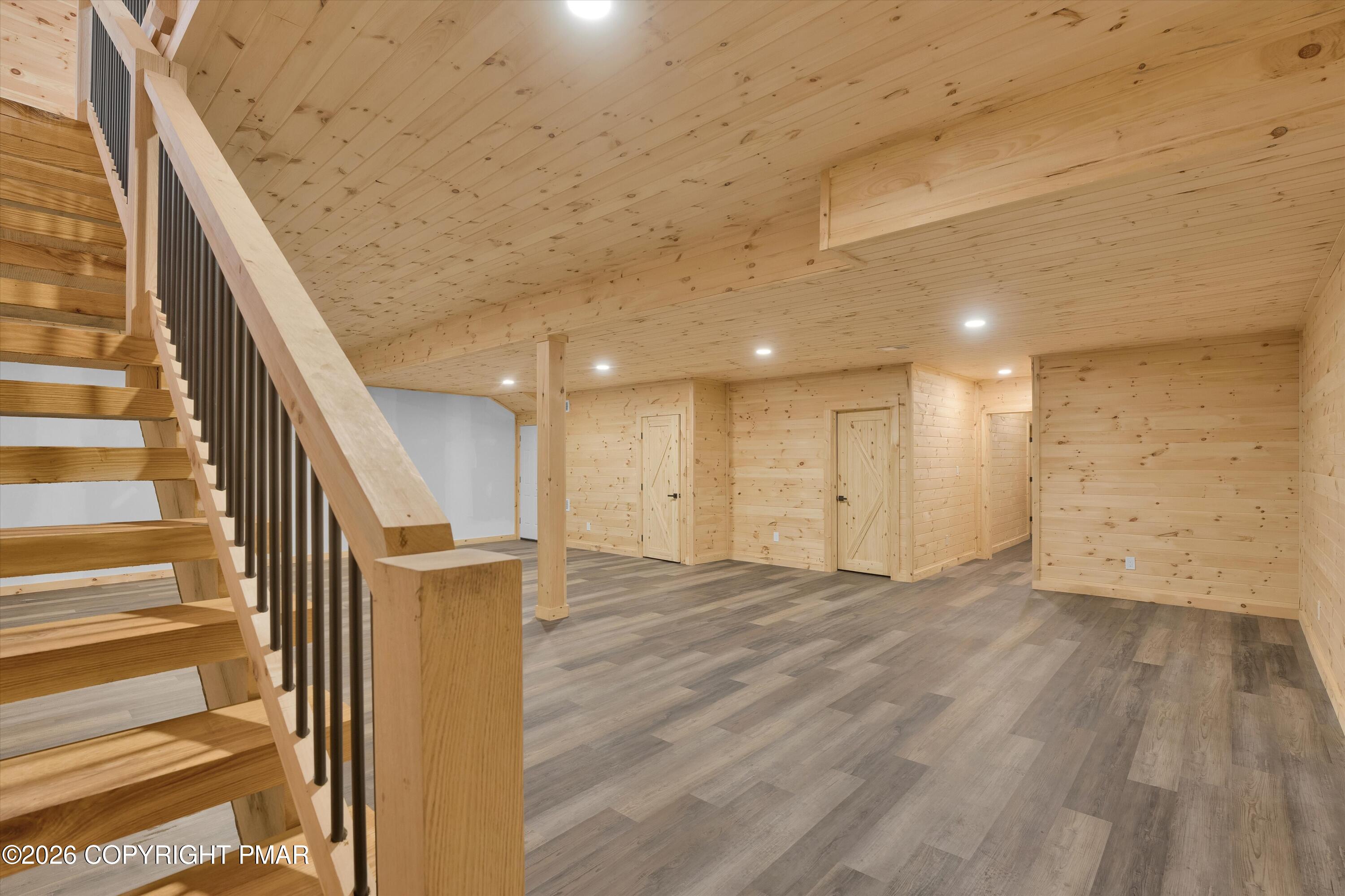 Finished basement with wood-paneled walls and ceiling, gray flooring, and an open wooden staircase.