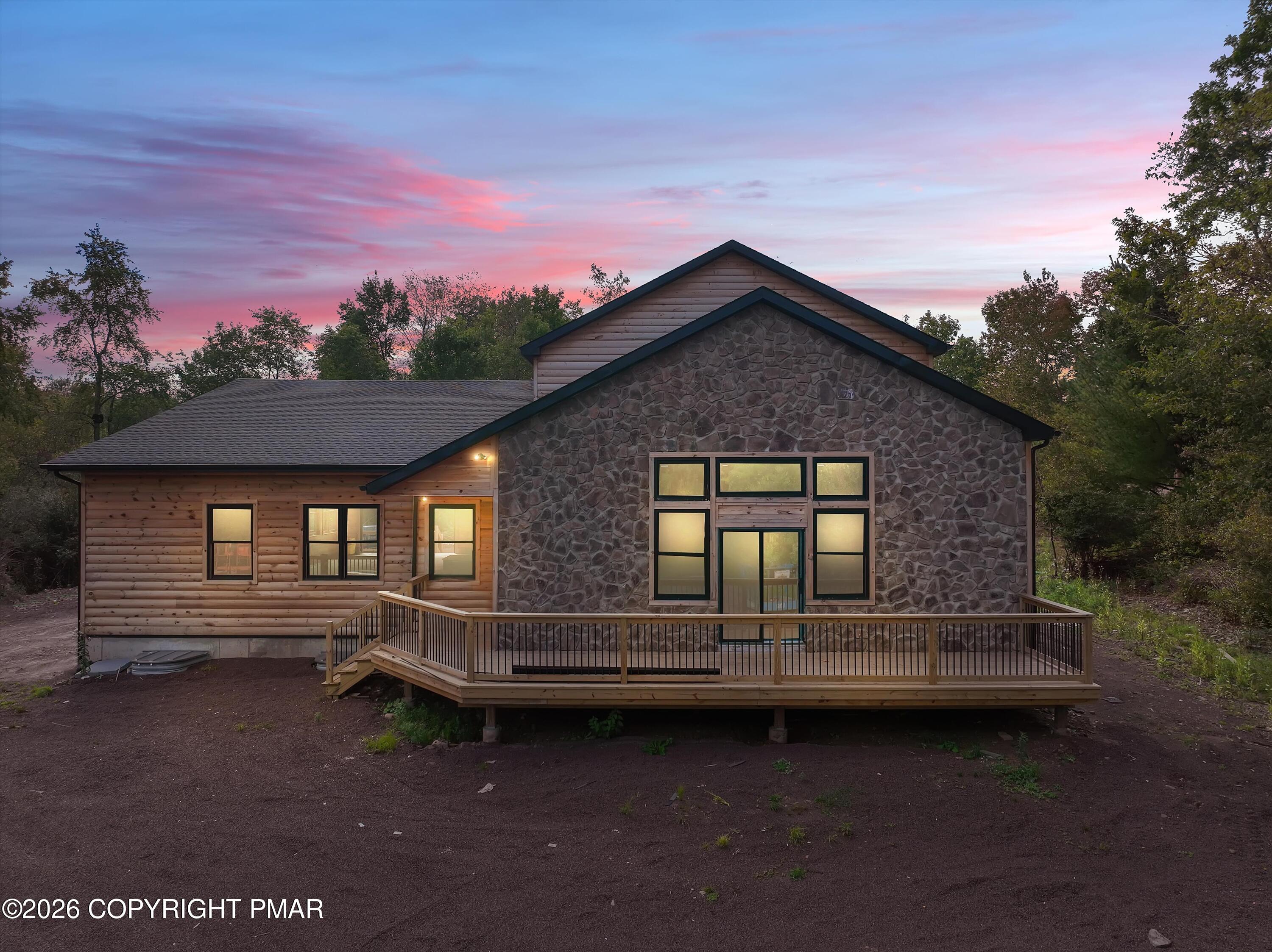 House with a stone facade and raised deck beneath a pink dusk sky.