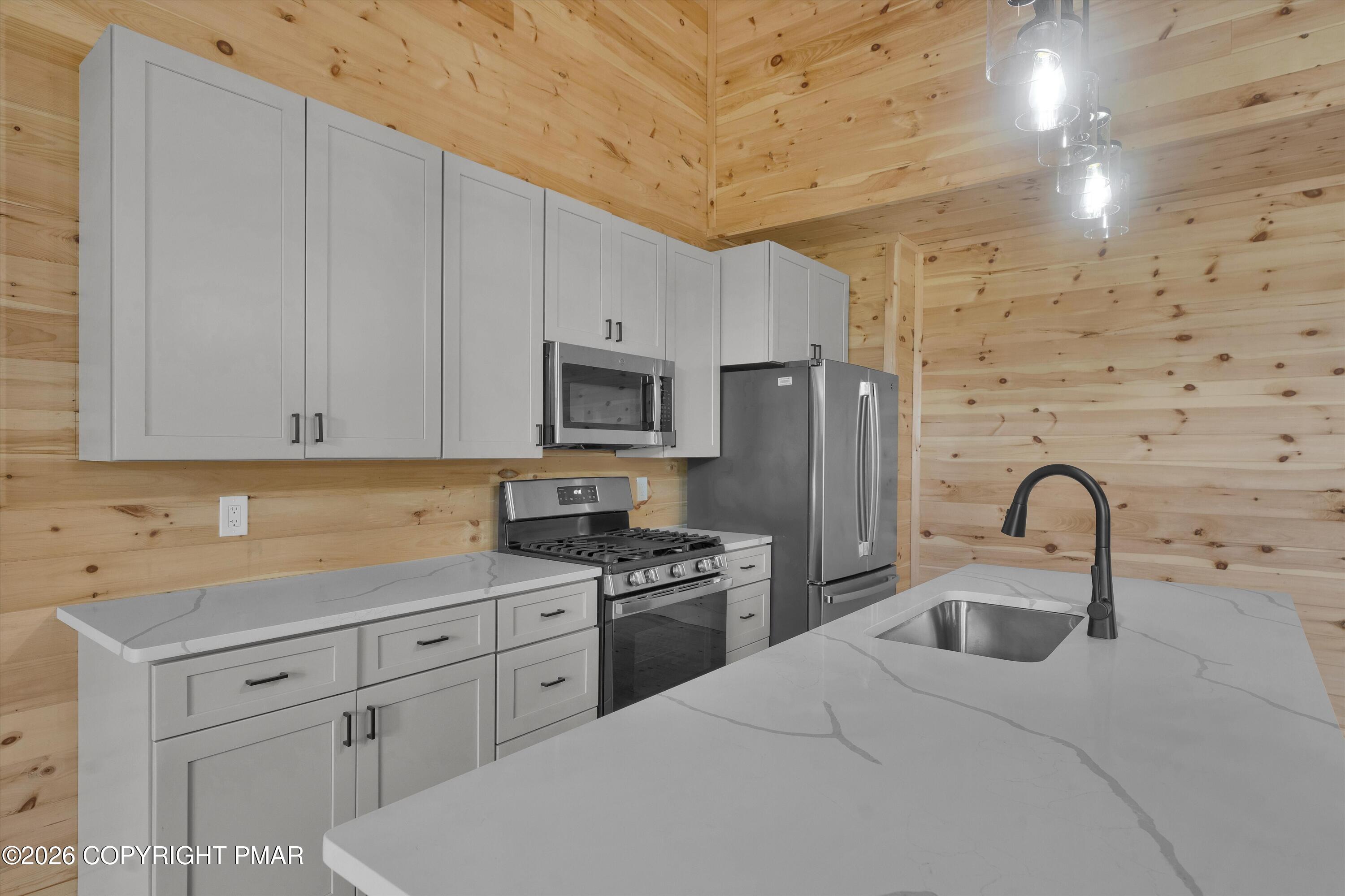 Kitchen with white cabinets, stainless steel appliances, and a quartz island against knotty pine walls.