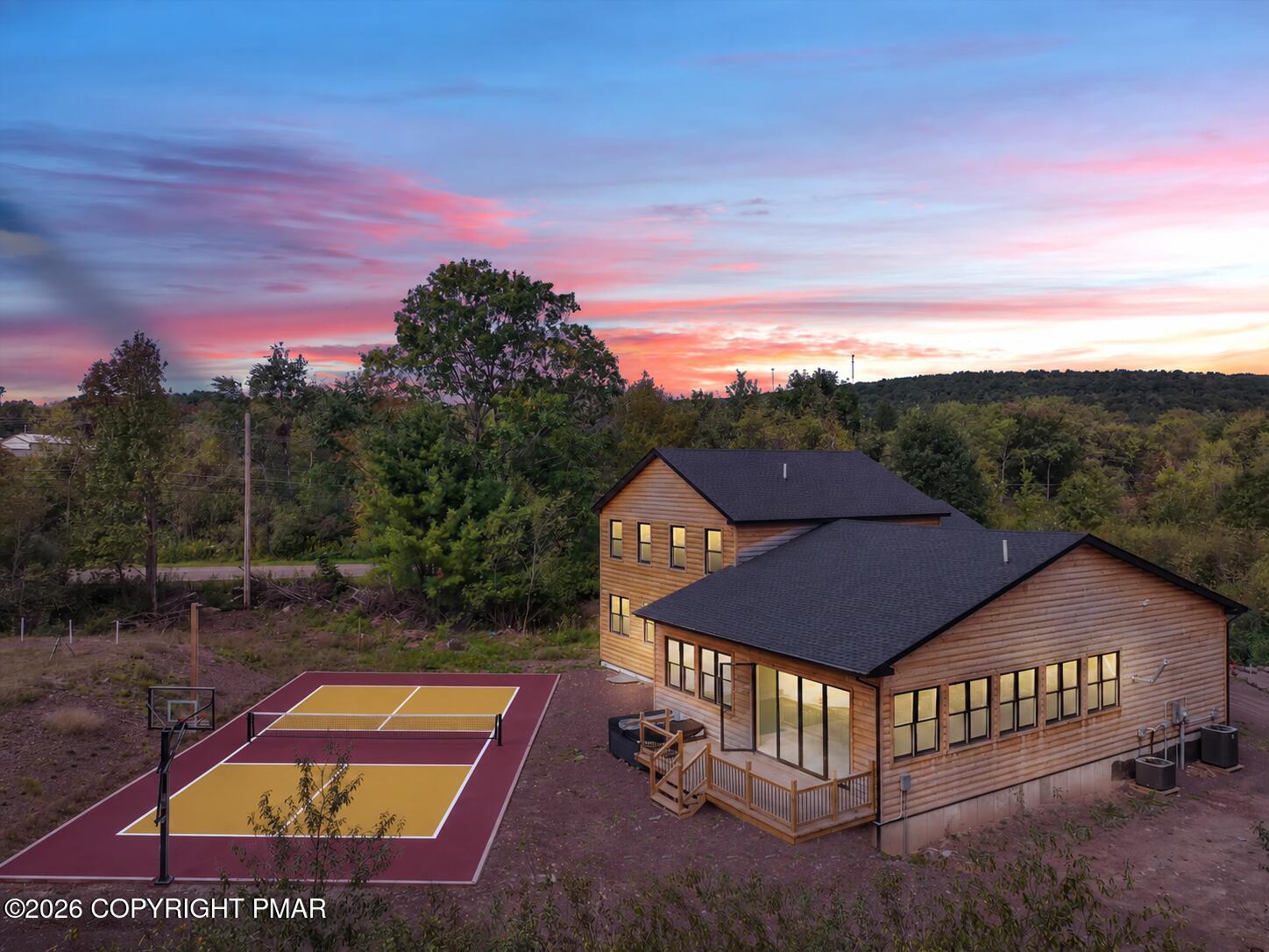 Wood-sided home beside a colorful outdoor sport court, surrounded by trees at sunset.