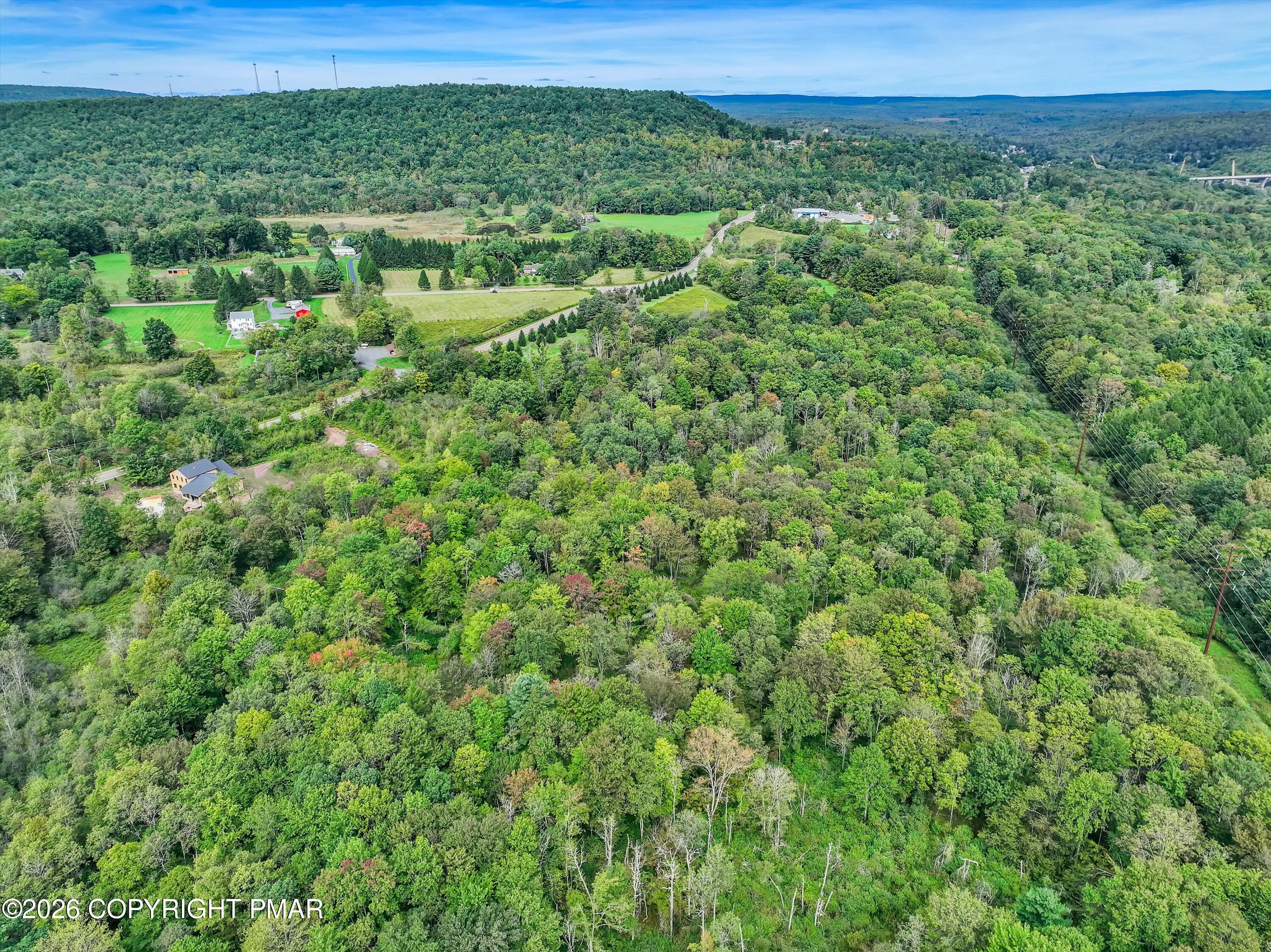 Aerial view of wooded rolling land with scattered homes, fields, and roads.