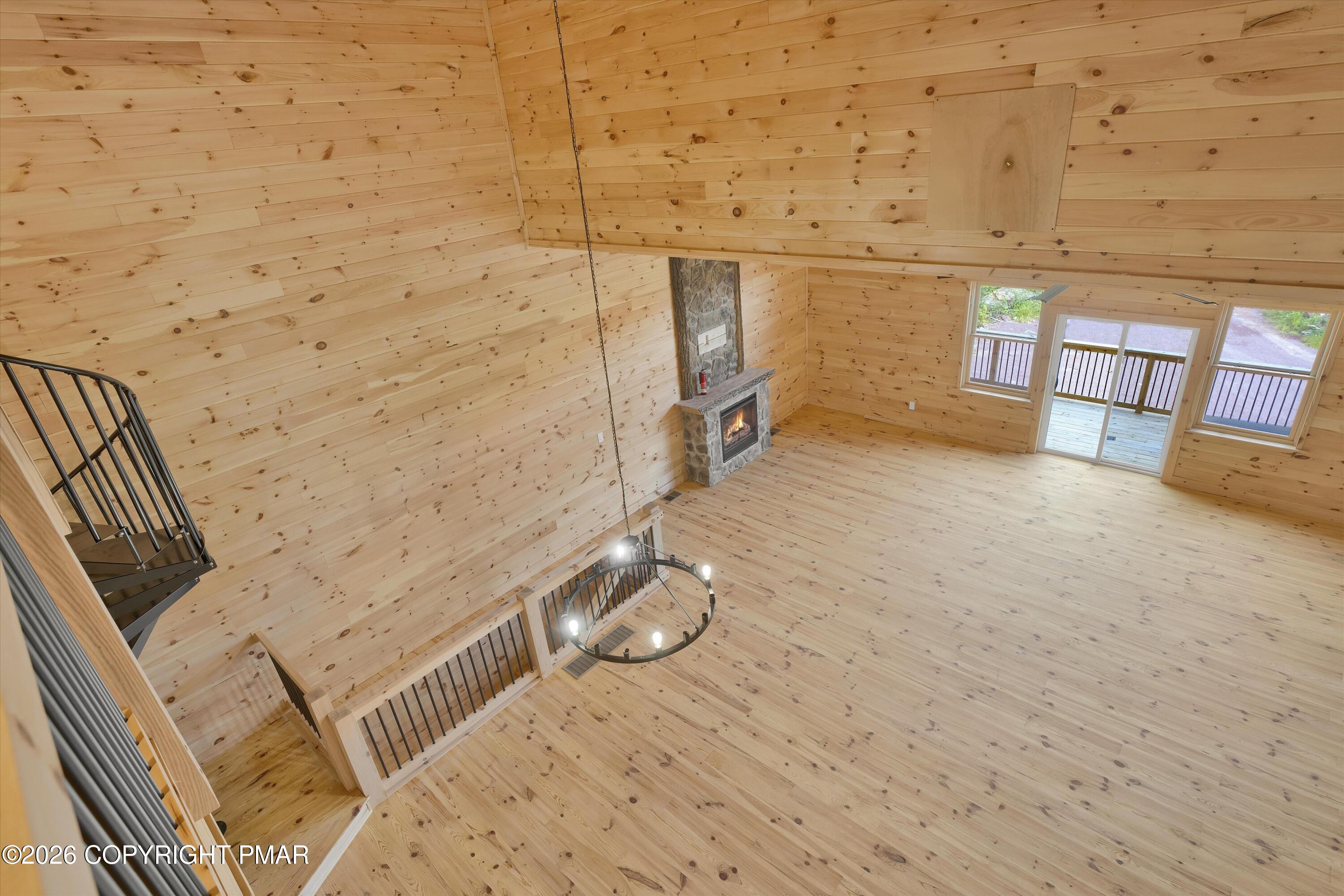 Wood-paneled great room with a vaulted ceiling, stone fireplace, staircase, and glass doors to a deck.