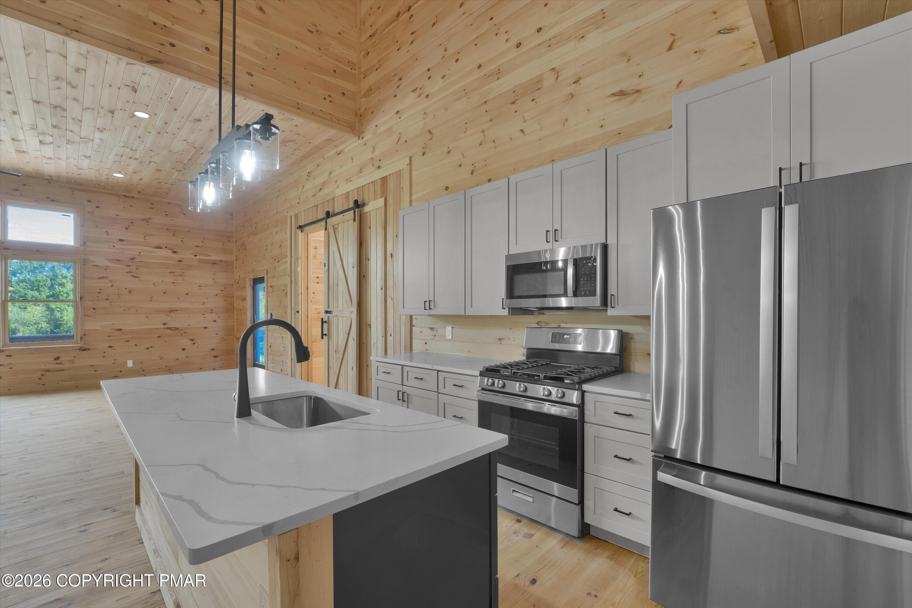 Kitchen with a white-veined island, stainless steel appliances, and natural wood walls and ceiling.
