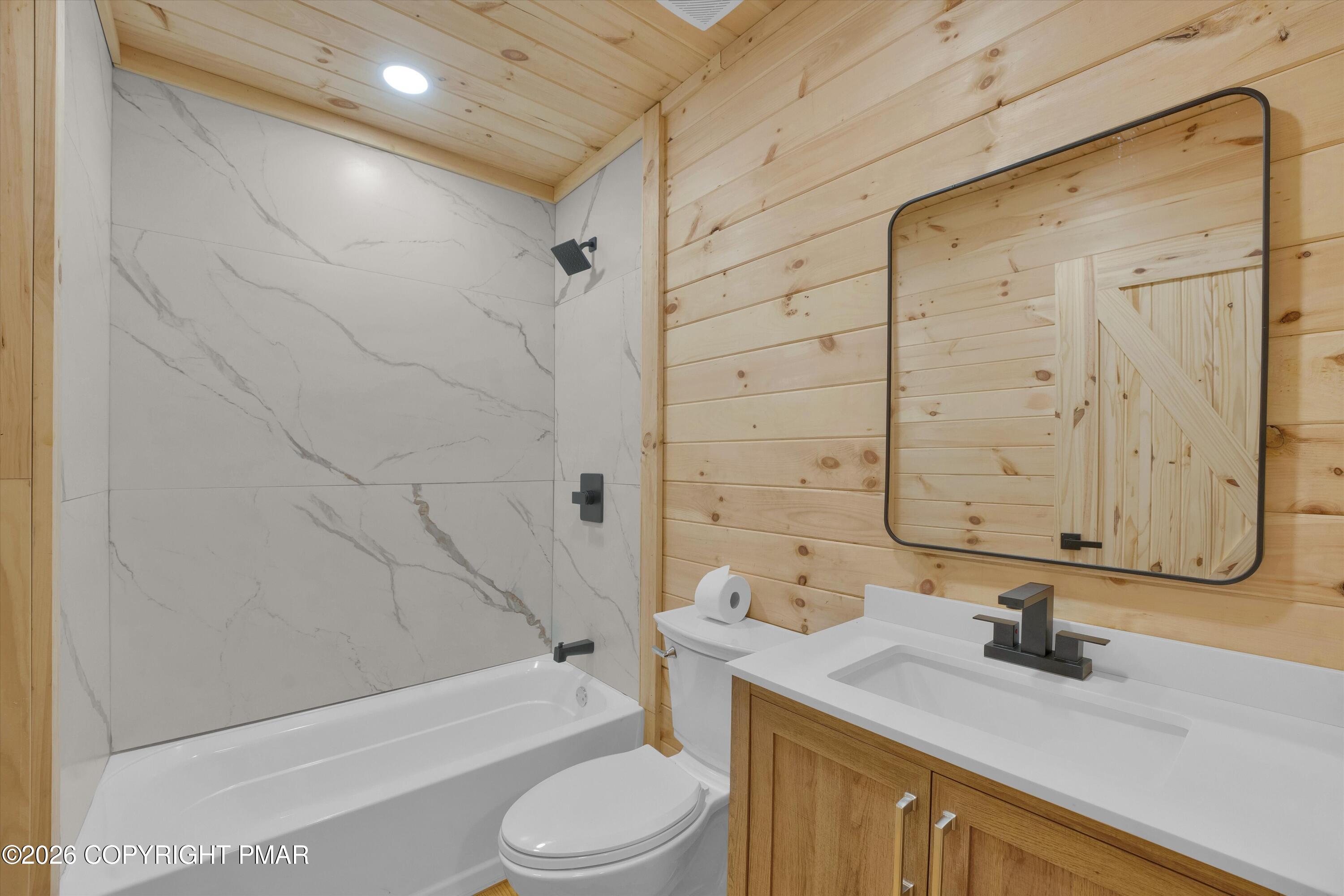 Bathroom with a marble-look tub surround, wood-clad walls, and a wood-front vanity.