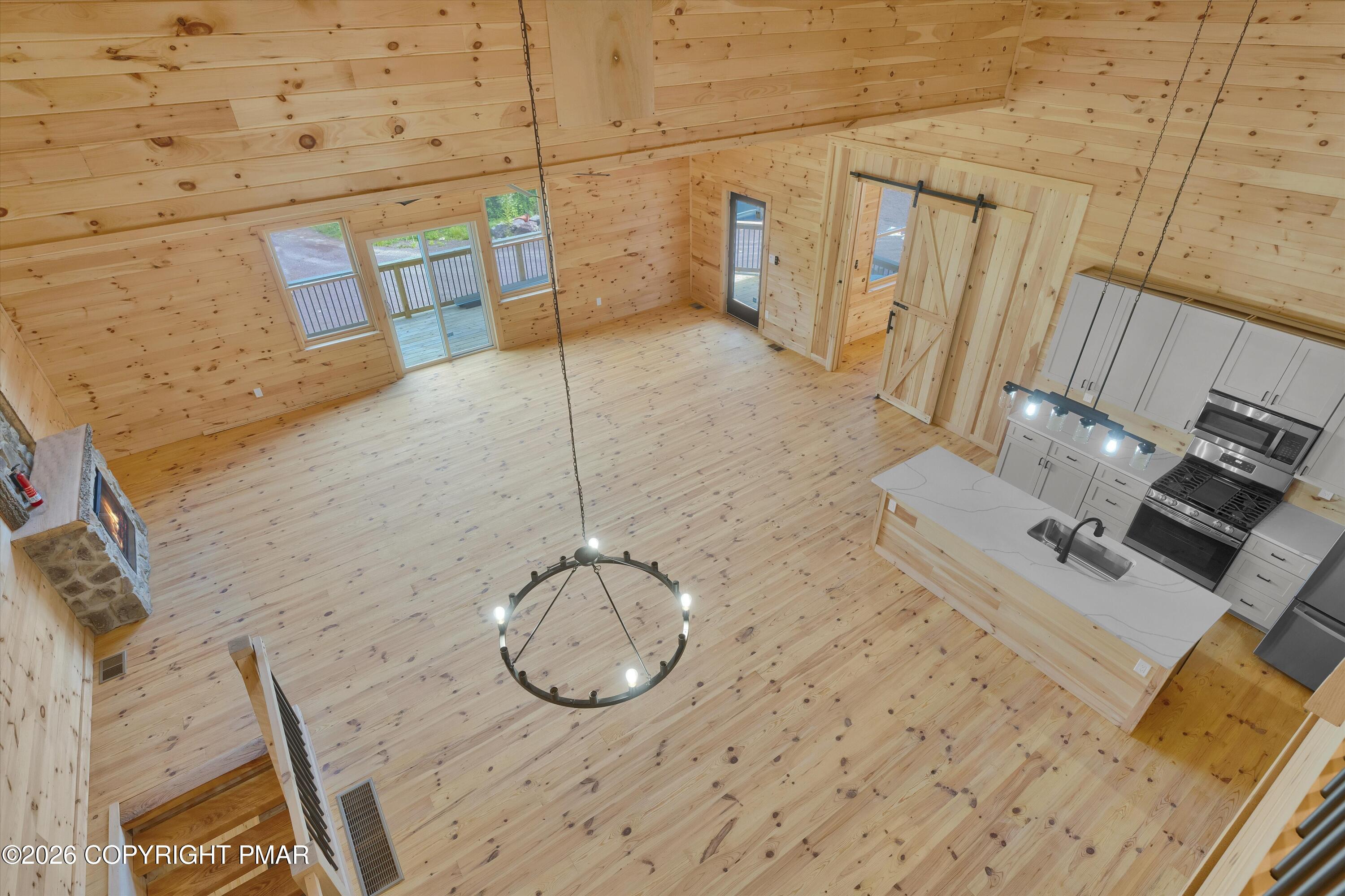 Open-plan great room with vaulted pine ceiling, stone fireplace, and white kitchen island.