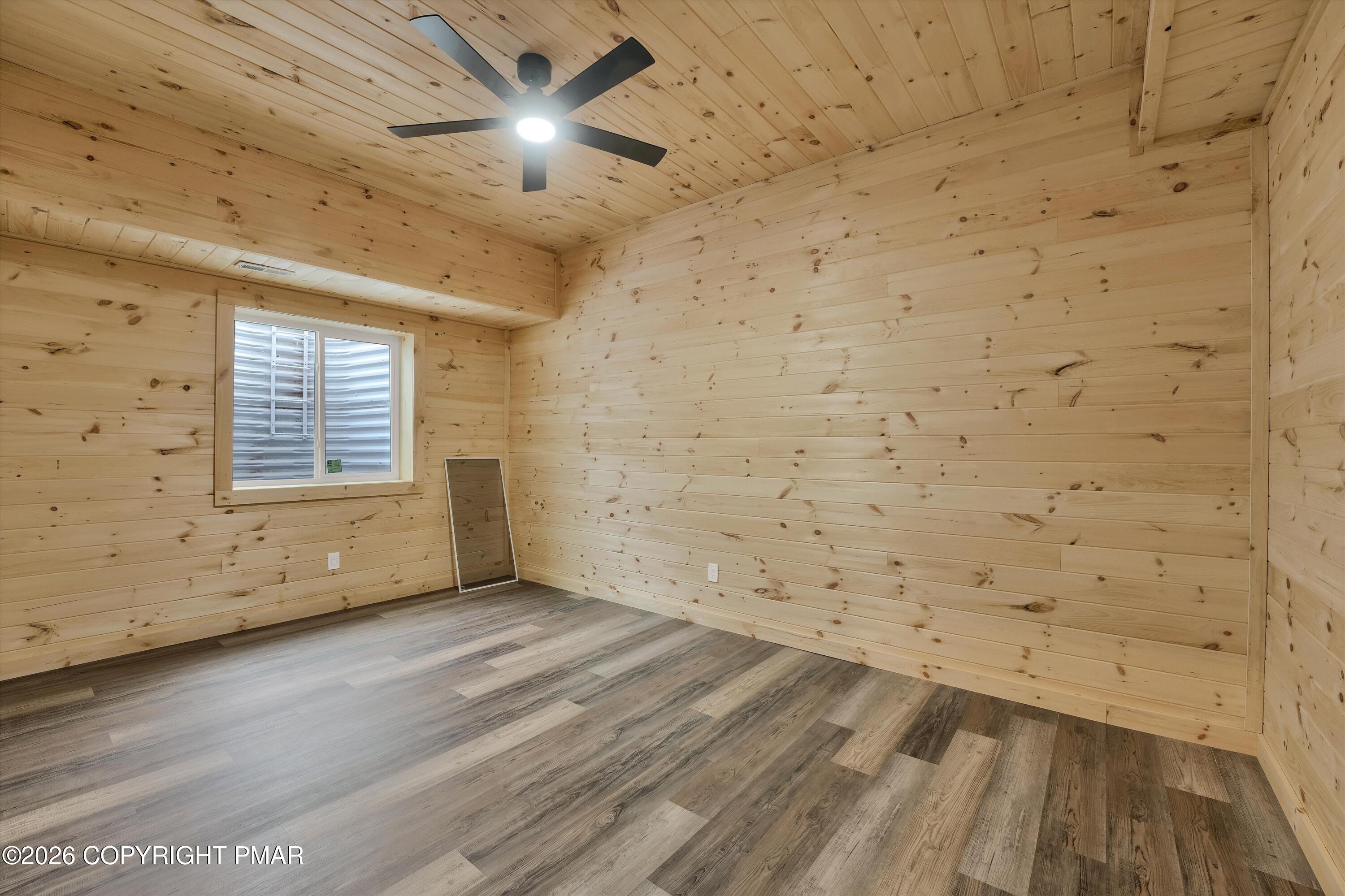 Empty wood-paneled room with gray-brown flooring, a window, and a ceiling fan.