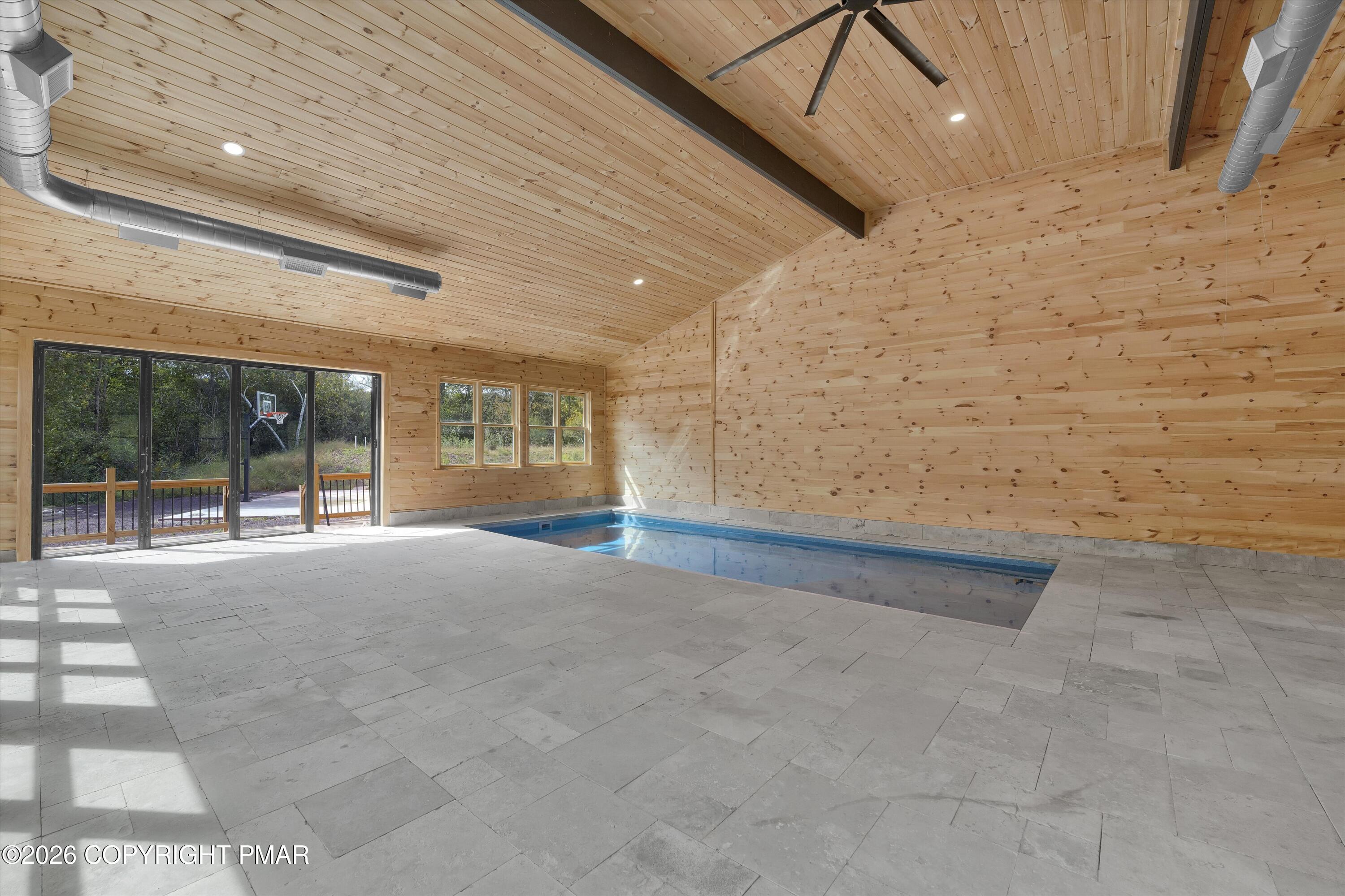 Indoor pool beneath a vaulted wood ceiling, with stone tile floors and sliding glass doors.