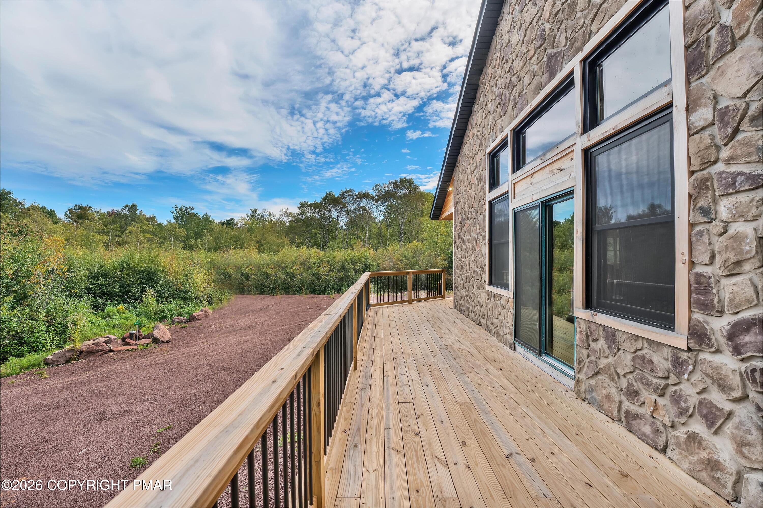 Stone-sided home with a long wooden deck overlooking a wooded yard.