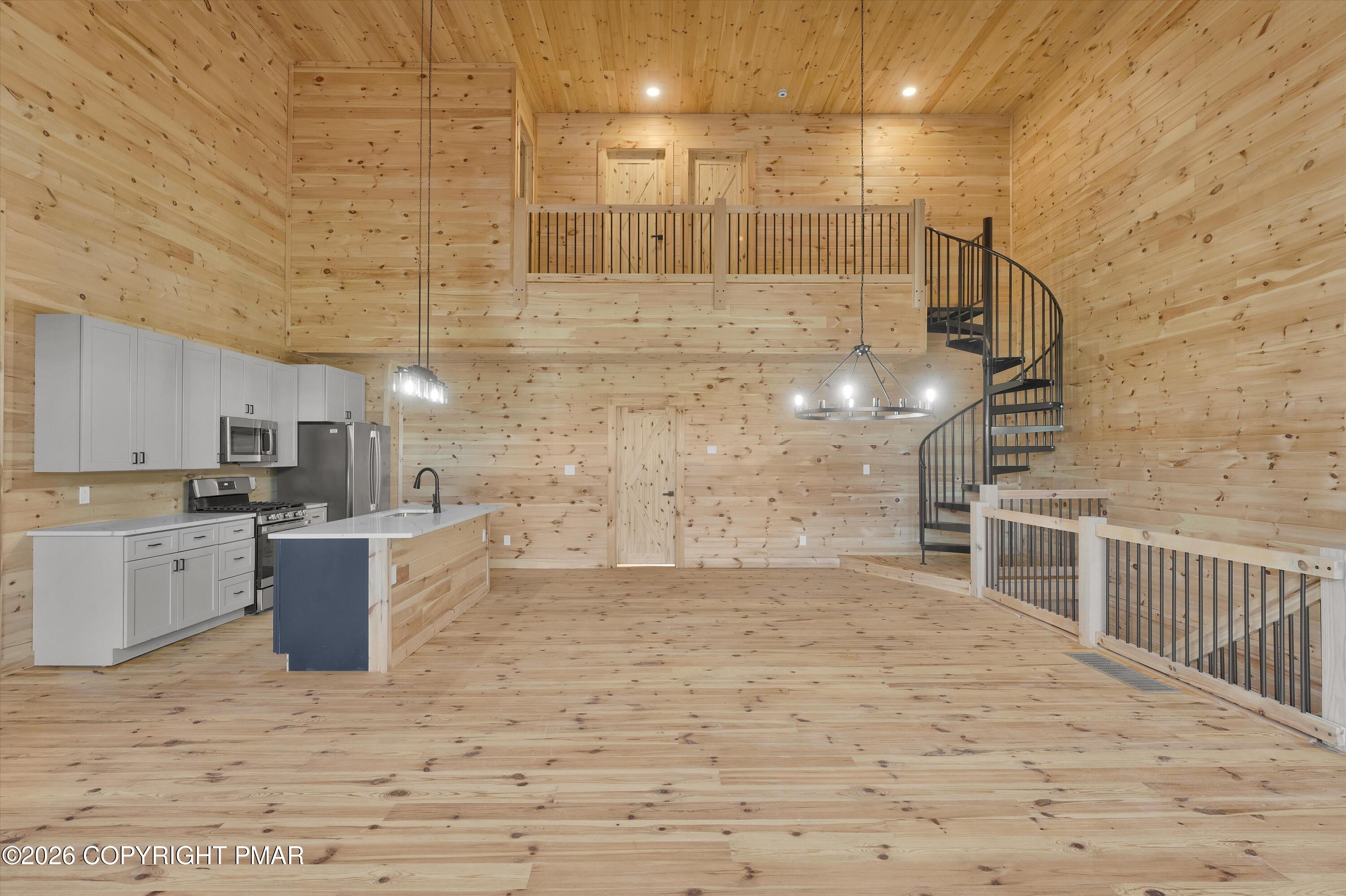 Open-plan pine interior with a gray-cabinet kitchen, black spiral staircase, and loft railing.
